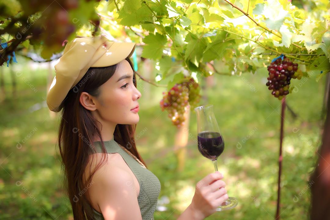 Mulher asiática com copo de vinho tinto no vinhedo em suas férias.