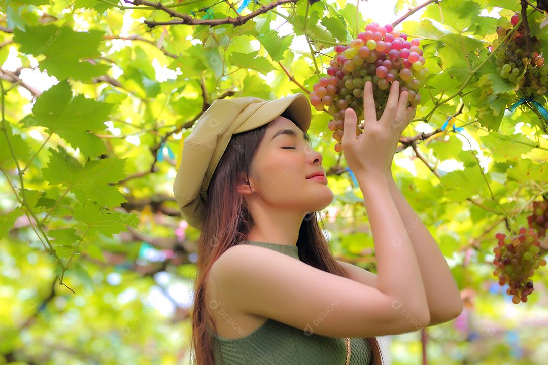 Mulher asiática segurando um cacho de uva em vinhedo.