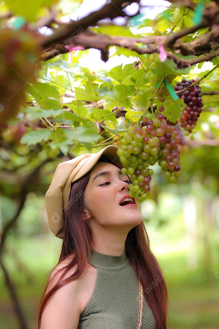 Mulher asiática segurando um cacho de uva em vinhedo.