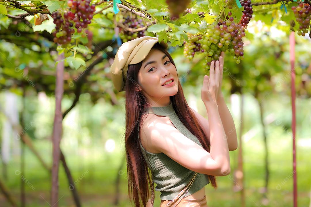 Mulher asiática segurando um cacho de uva em vinhedo.