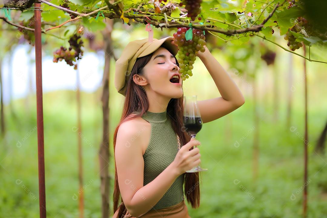Mulher asiática segurando um cacho de uva em vinhedo.