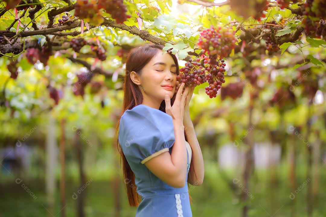 Mulher asiática segurando um cacho de uva em um vinhedo.