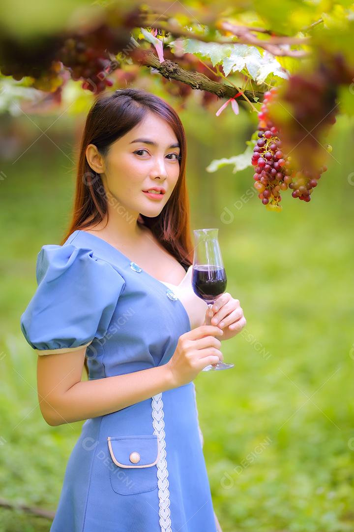 Mulher asiática com copo de vinho tinto no vinhedo em suas férias.
