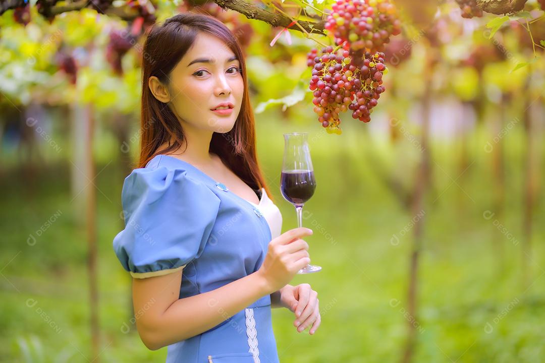 Mulher asiática com copo de vinho tinto no vinhedo em suas férias.