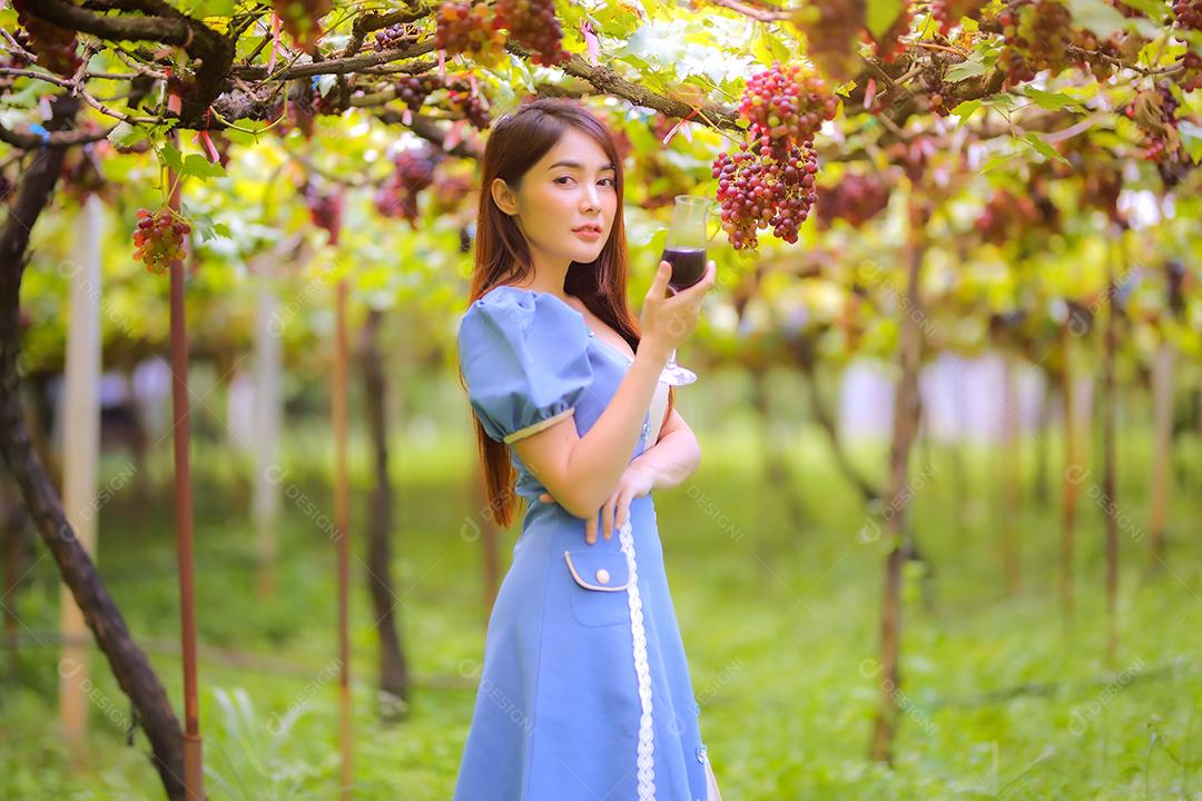 Mulher asiática com copo de vinho tinto no vinhedo em suas férias.