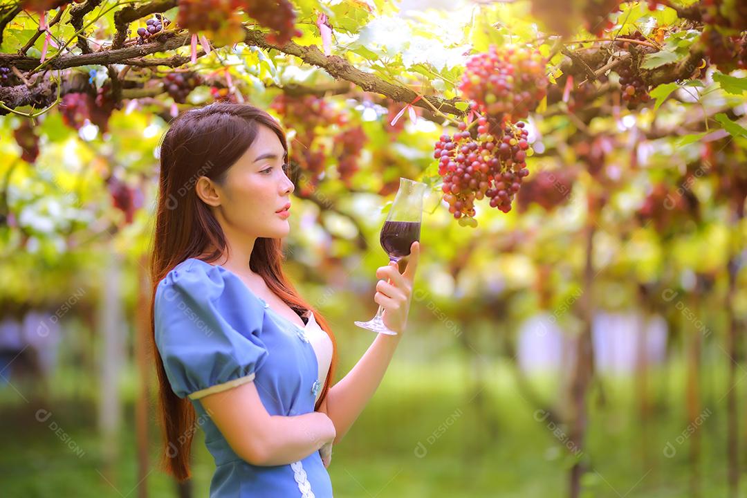 Mulher asiática com copo de vinho tinto no vinhedo em suas férias.