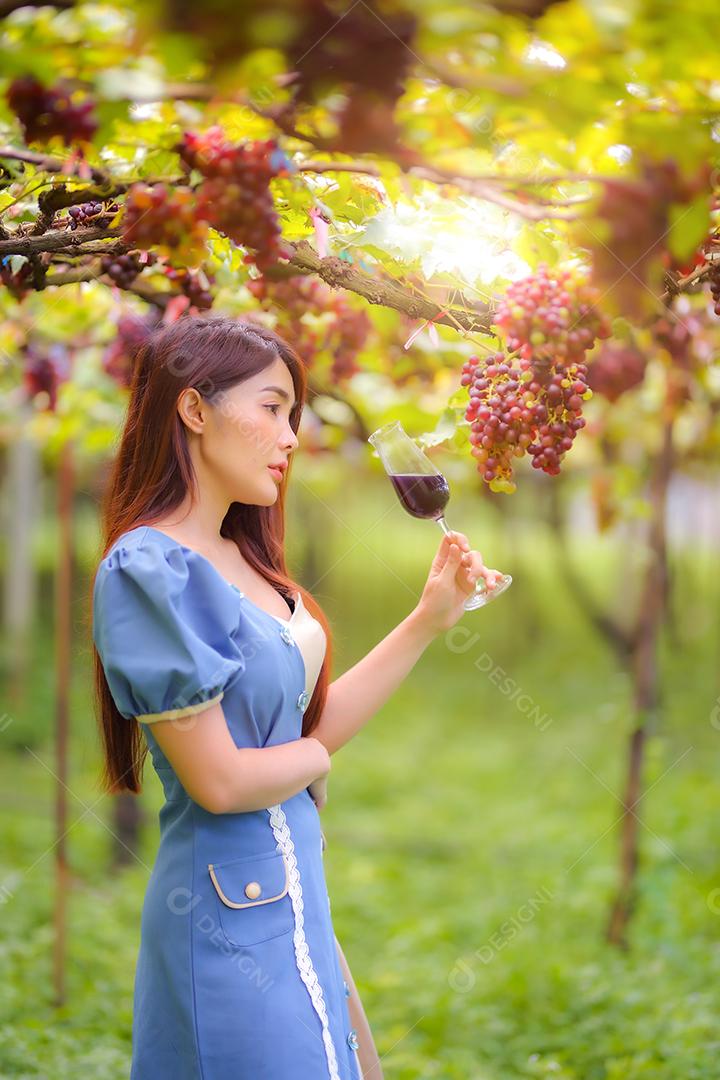 Mulher asiática com copo de vinho tinto no vinhedo em suas férias.