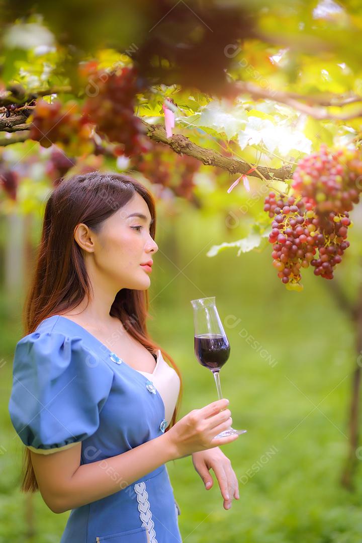 Mulher asiática com copo de vinho tinto no vinhedo em suas férias.