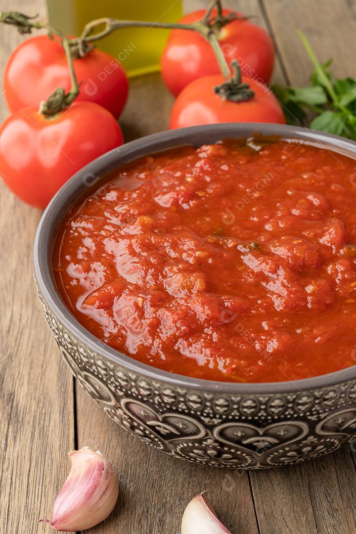 Molho de tomate, tomate, alho, azeite e ervas sobre a mesa de madeira.