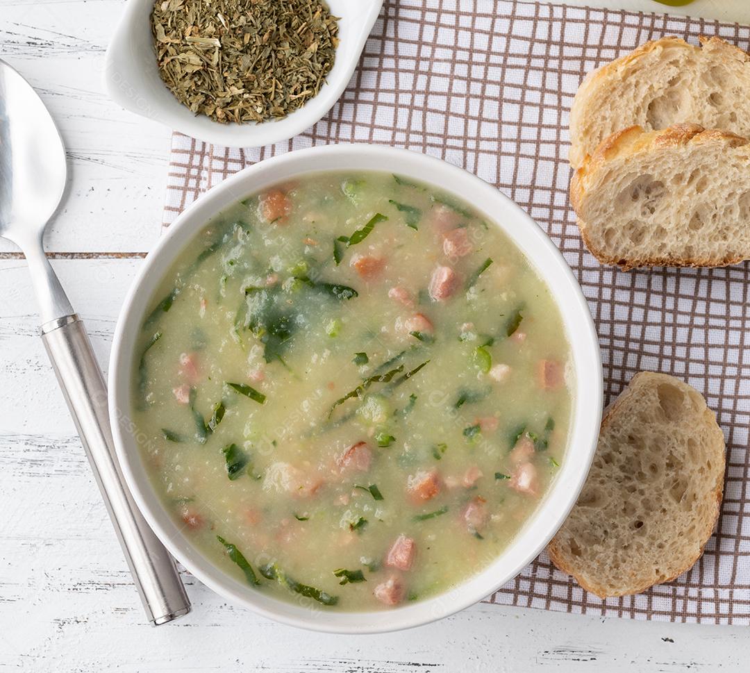 Sopa verde tradicional portuguesa com batata, couve verde e salsicha numa tigela com pão.