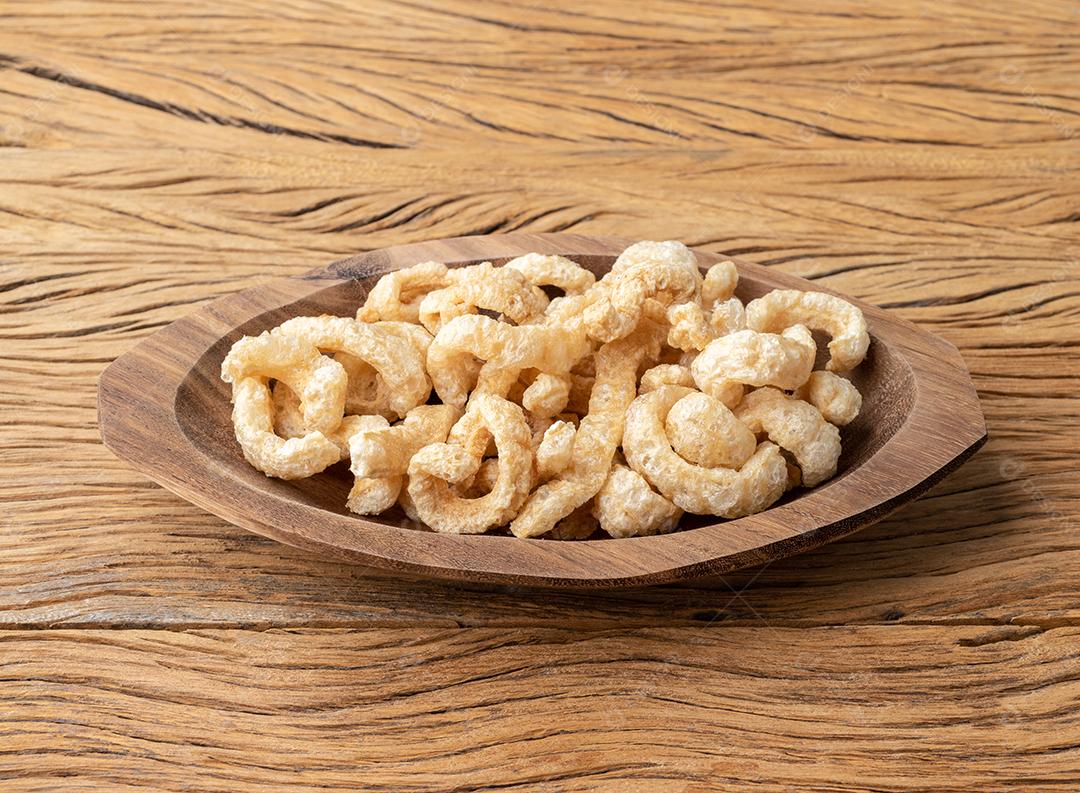 Torresmo de pele de porco frito em um prato sobre a mesa de madeira.