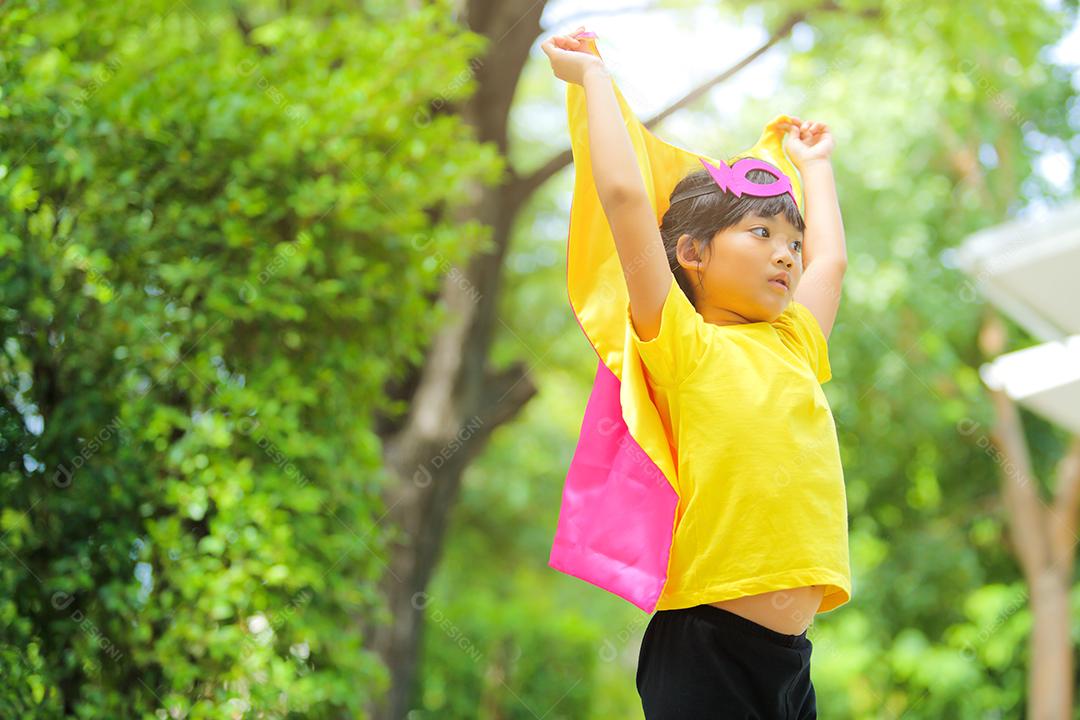 Uma menina bonitinha com máscara vestida e vestindo e capa de criança super-herói.