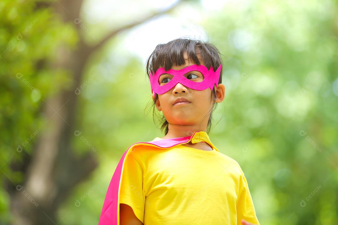 Uma menina bonitinha com máscara vestida e vestindo e capa de criança super-herói.