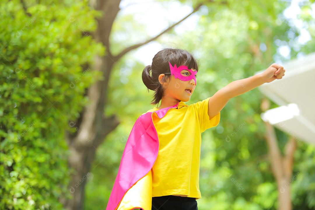 Uma menina bonitinha com máscara vestida e vestindo e capa de criança super-herói.