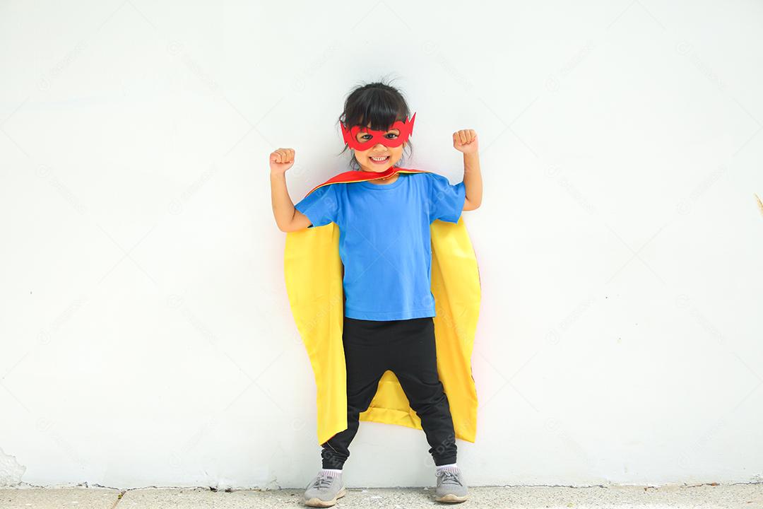 Uma menina bonitinha com máscara vestida e vestindo e capa de criança super-herói.