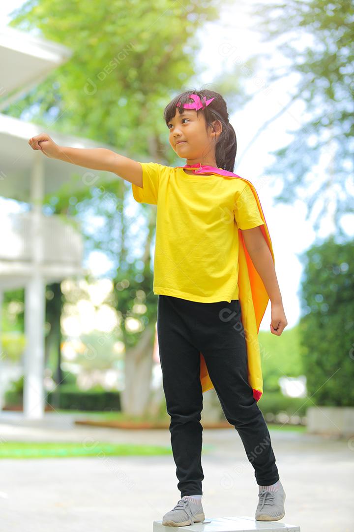 Uma menina bonitinha com máscara vestida e vestindo e capa de criança super-herói.