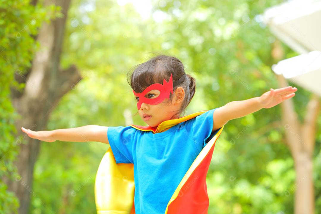 Uma menina bonitinha com máscara vestida e vestindo e capa de criança super-herói.