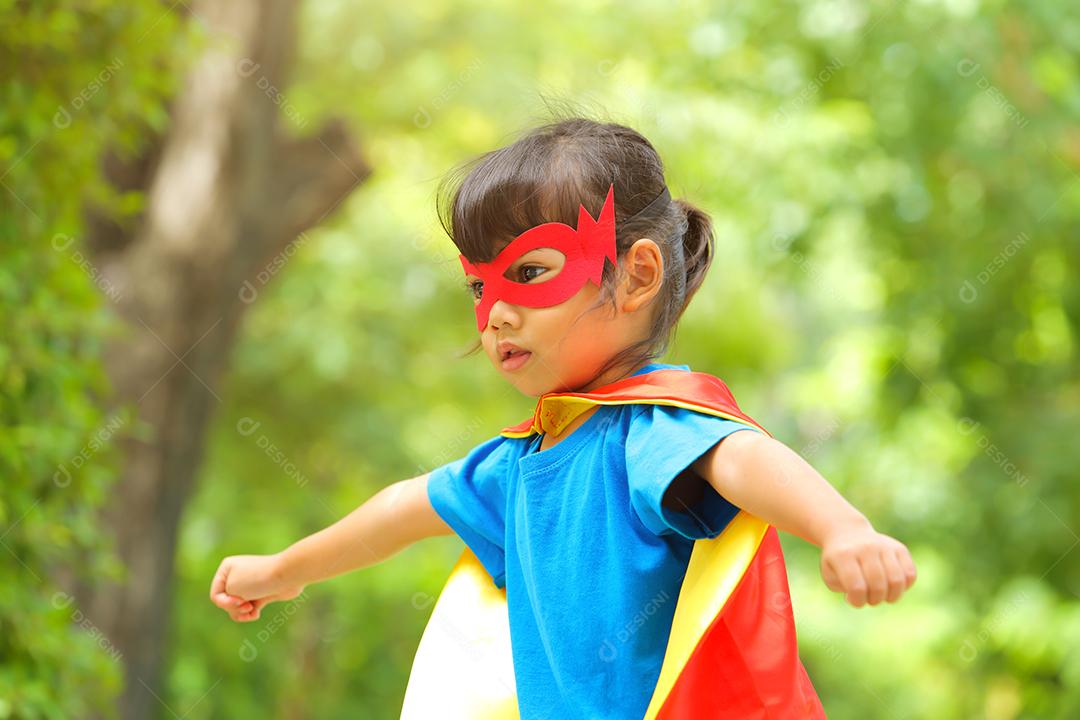 Uma menina bonitinha com máscara vestida e vestindo e capa de criança super-herói.