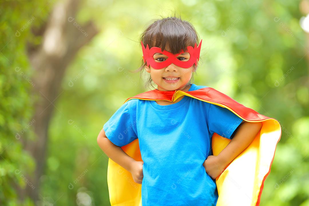 Uma menina bonitinha com máscara vestida e vestindo e capa de criança super-herói.