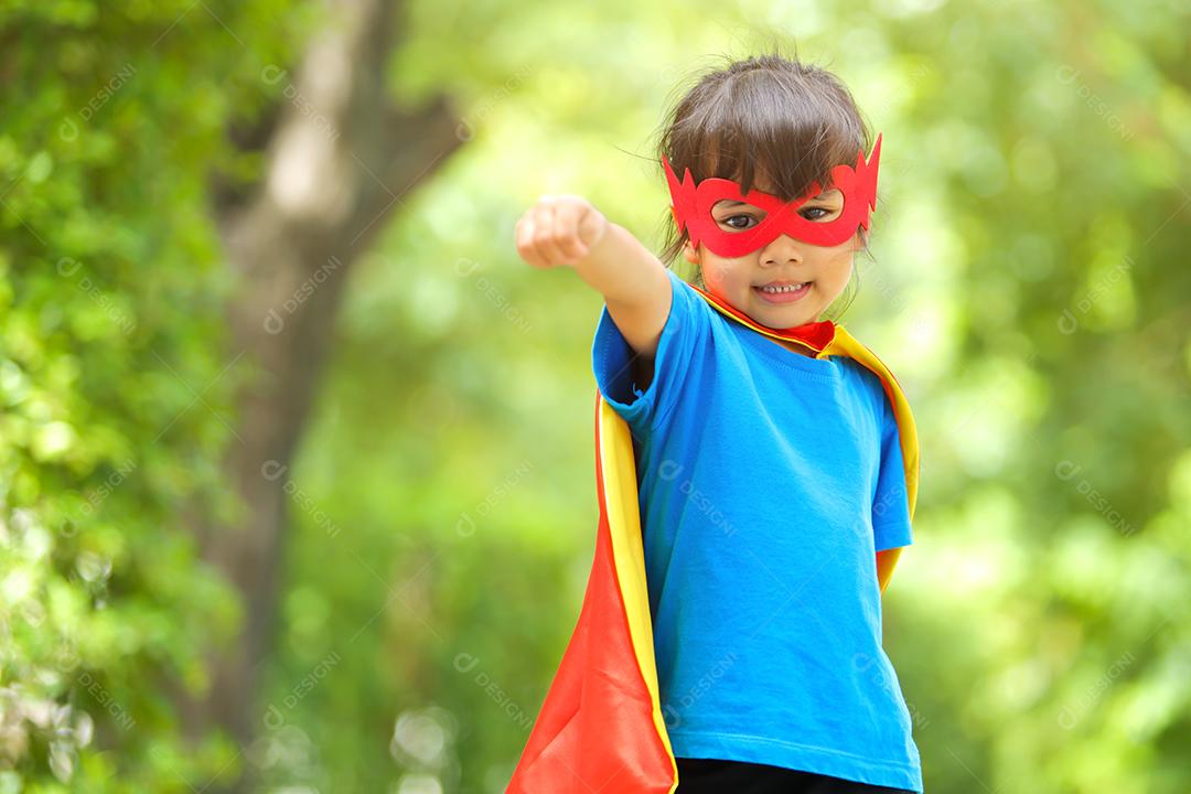 Uma menina bonitinha com máscara vestida e vestindo e capa de criança super-herói.