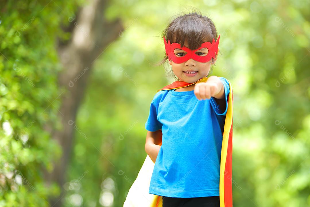 Uma menina bonitinha com máscara vestida e vestindo e capa de criança super-herói.