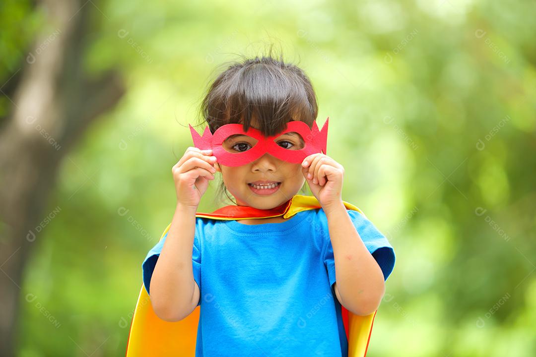 Uma menina bonitinha com máscara vestida e vestindo e capa de criança super-herói.