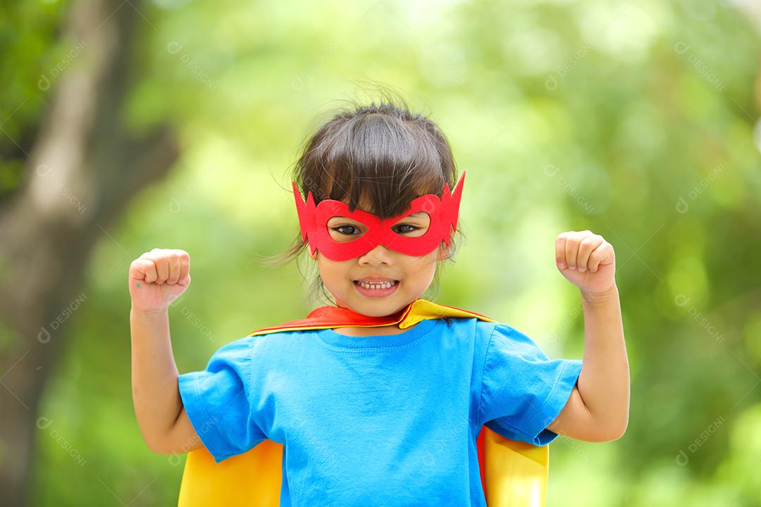 Uma menina bonitinha com máscara vestida e vestindo e capa de criança super-herói.