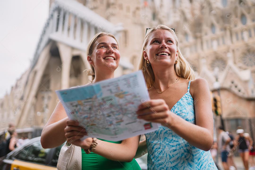 Amigas felizes aproveitando sua viagem em Barcelona segurando um mapa.