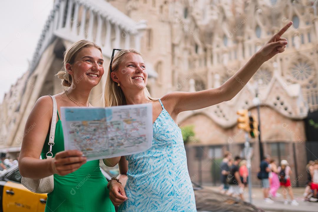 Amigas felizes aproveitando sua viagem em Barcelona segurando um mapa.