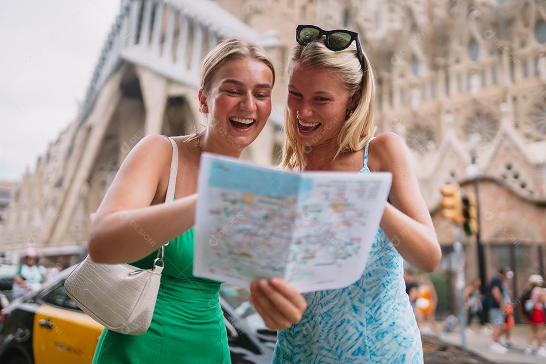 Amigas felizes aproveitando sua viagem em Barcelona segurando um mapa.