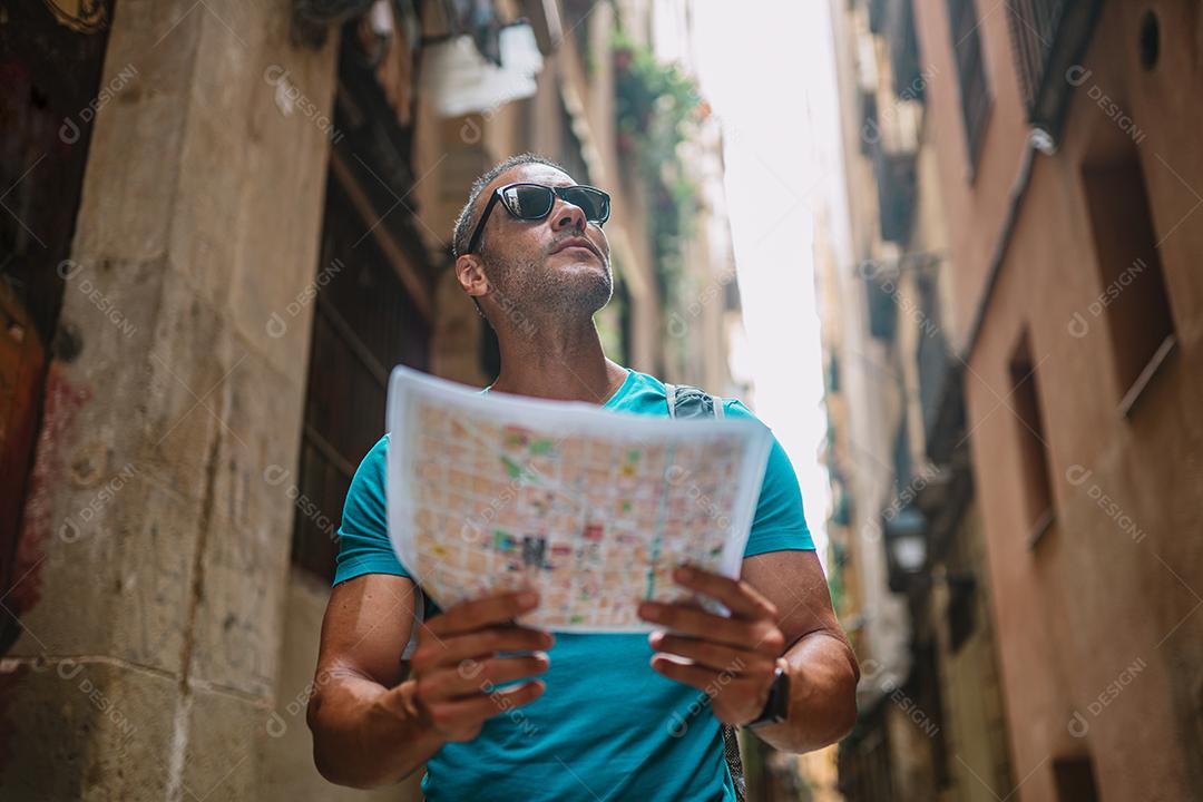 Feliz usuário de mapas turísticos masculinos andando no beco da cidade velha e usando