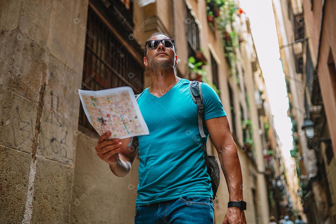 Feliz usuário de mapas turísticos masculinos andando no beco da cidade velha e usando