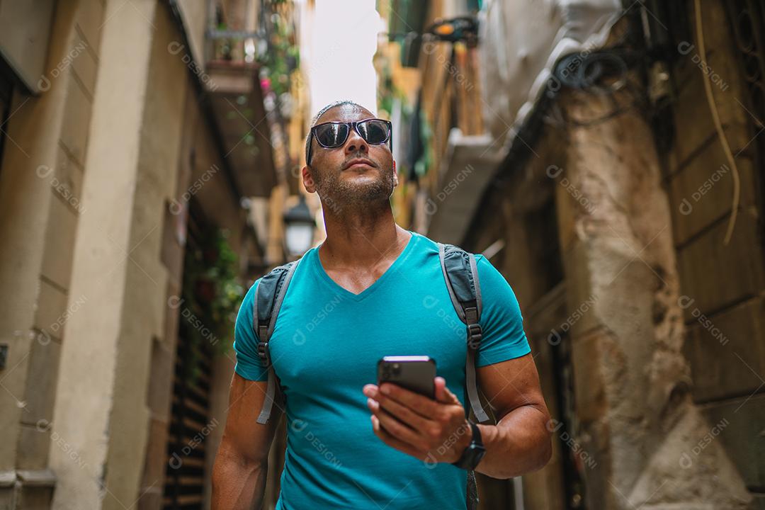 Feliz usuário de telefone turístico masculino andando no beco da cidade velha e usando