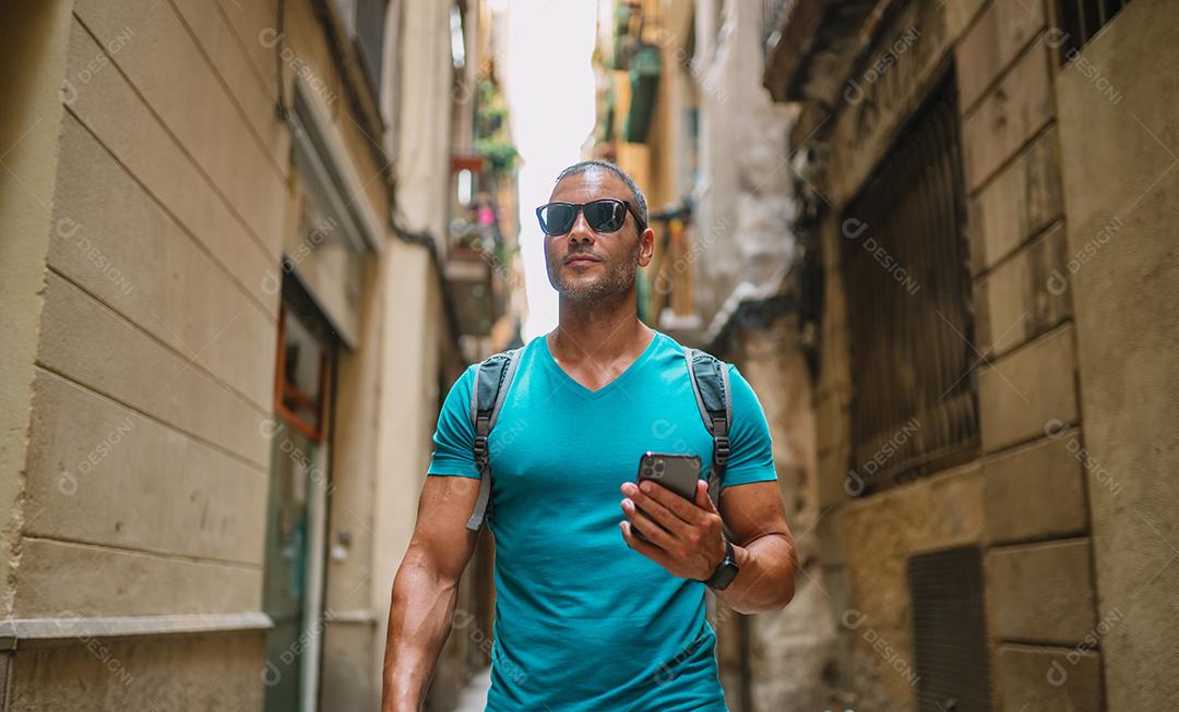 Feliz usuário de telefone turístico masculino andando no beco da cidade velha e usando