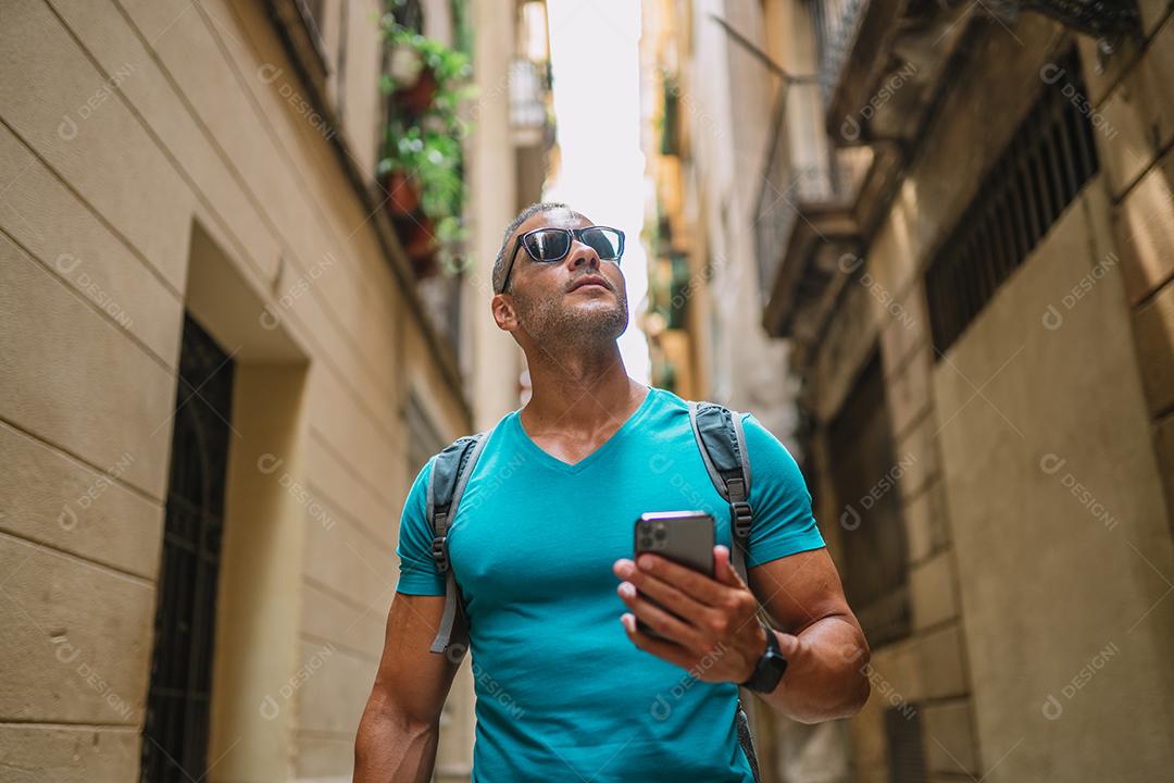 Feliz usuário de telefone turístico masculino andando no beco da cidade velha e usando