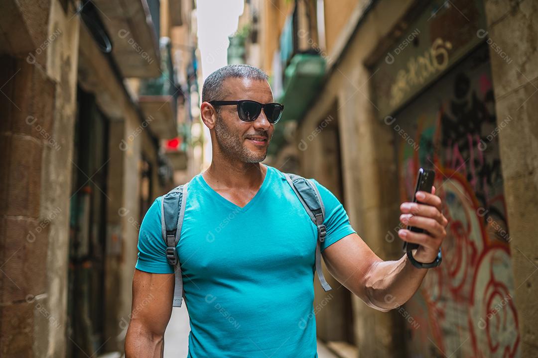 Feliz usuário de telefone turístico masculino andando no beco da cidade velha e usando