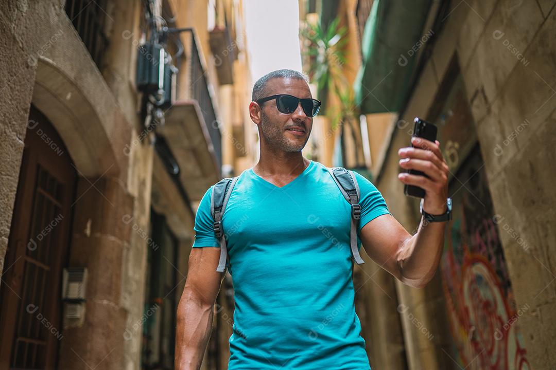 Feliz usuário de telefone turístico masculino andando no beco da cidade velha e usando