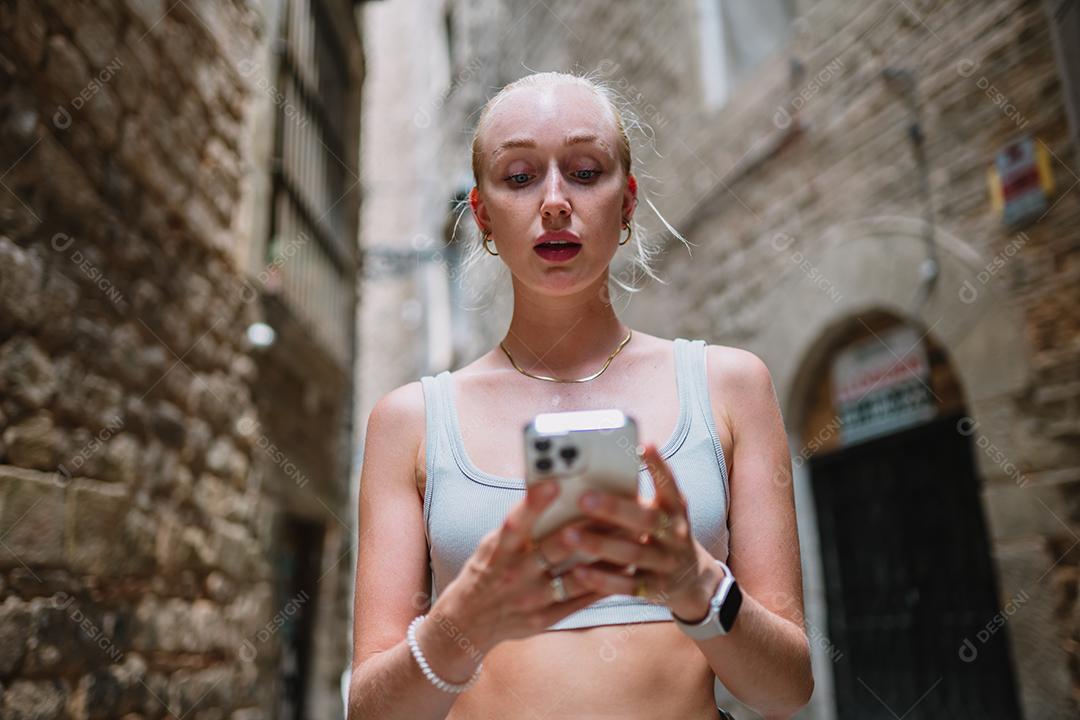 Feliz usuário de telefone turístico feminino andando no beco da cidade velha.