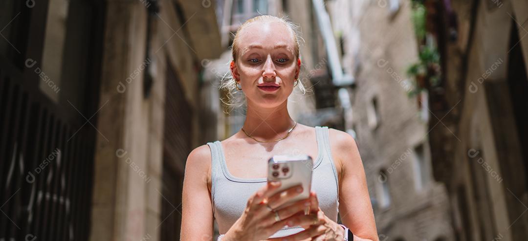Feliz usuário de telefone turístico feminino andando no beco da cidade velha.