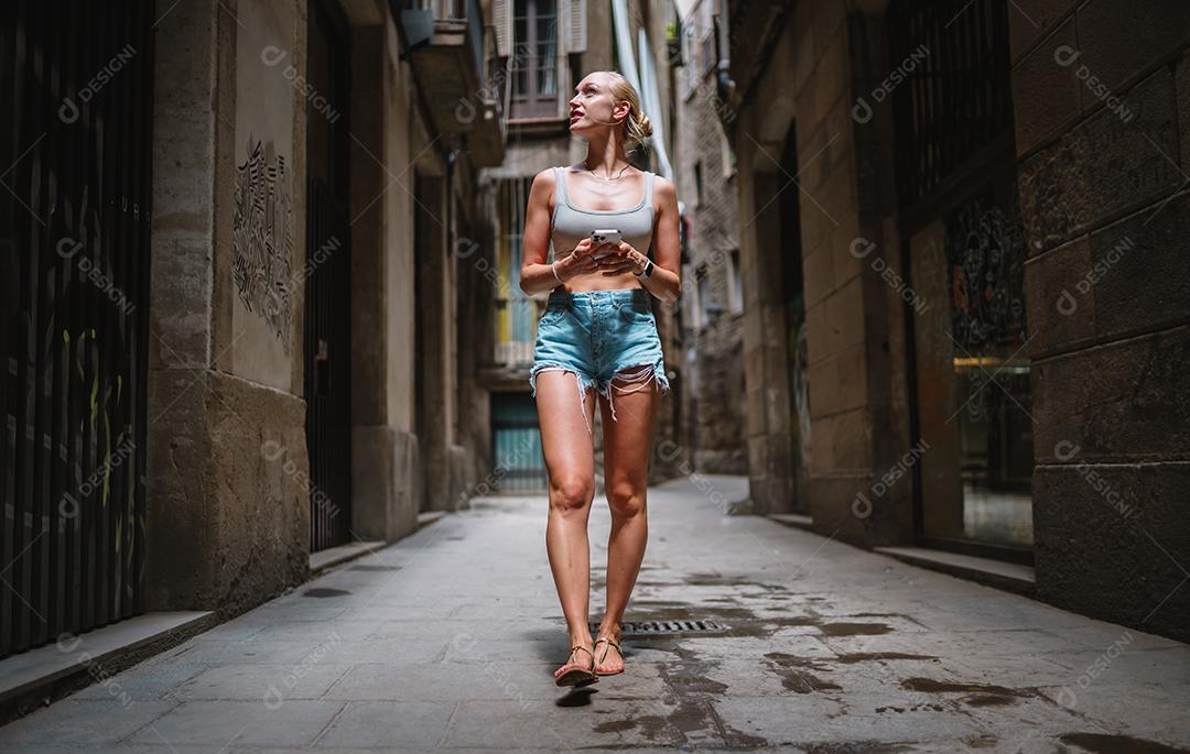 Feliz usuário de telefone turístico feminino andando no beco da cidade velha.