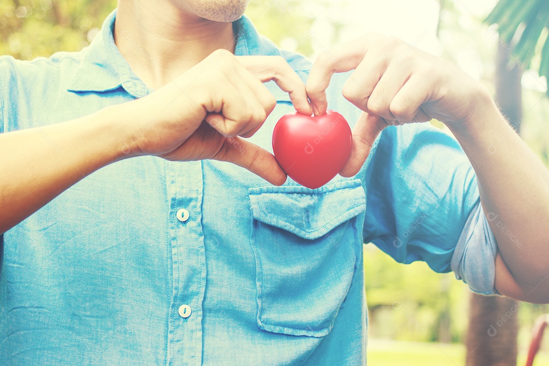 O homem na camisa azul segura nas mãos o coração vermelho no fundo da grama verde