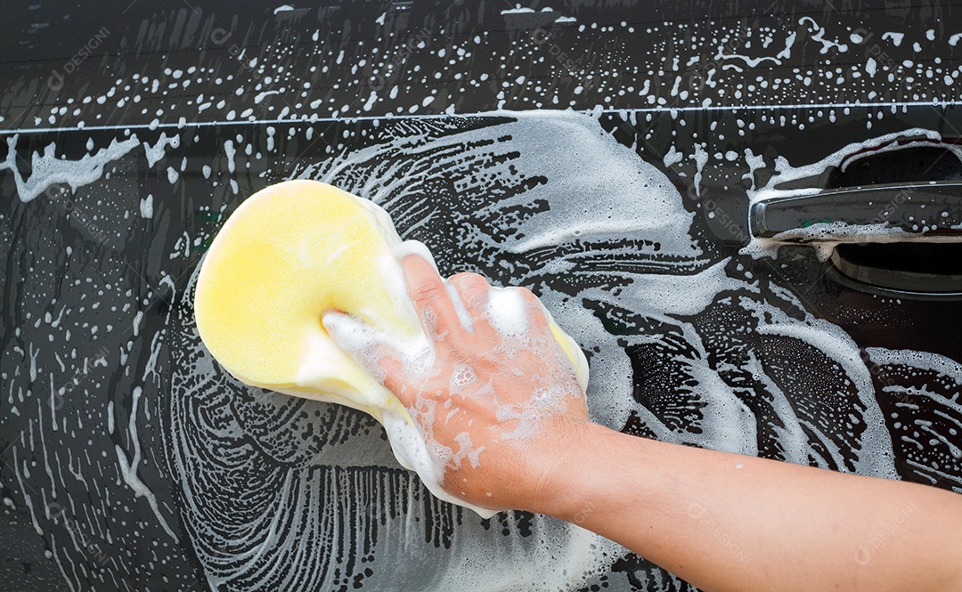 mão do homem lavando o carro usando a esponja amarela com espuma