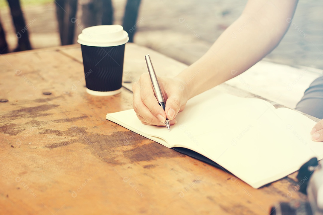 Mãos com caneta escrevendo no caderno com café