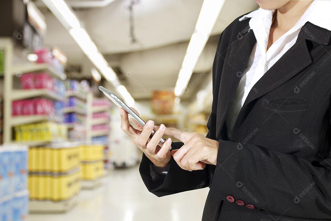 Empresário e mulher estão usando telefone inteligente móvel e sensível ao toque para comunicação e verificando o fundo do supermercado/shopping, foco seletivo na mão