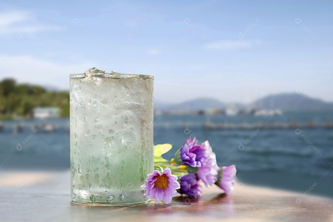 copo de água e flor falsa na mesa de madeira no fundo da vista para o mar