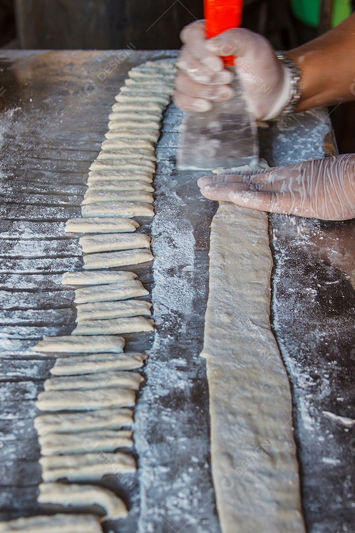 Mãos de mulher cortando massa em uma mesa com farinha