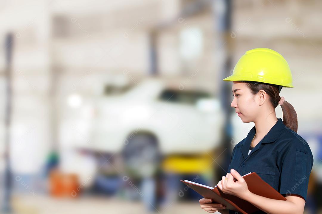Retrato de uma jovem mecânica sorridente inspecionando um carro na oficina de automóveis