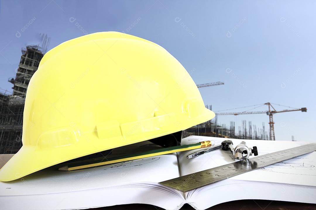 capacete com bússolas de lápis e réguas/livro na mesa no fundo do canteiro de obras