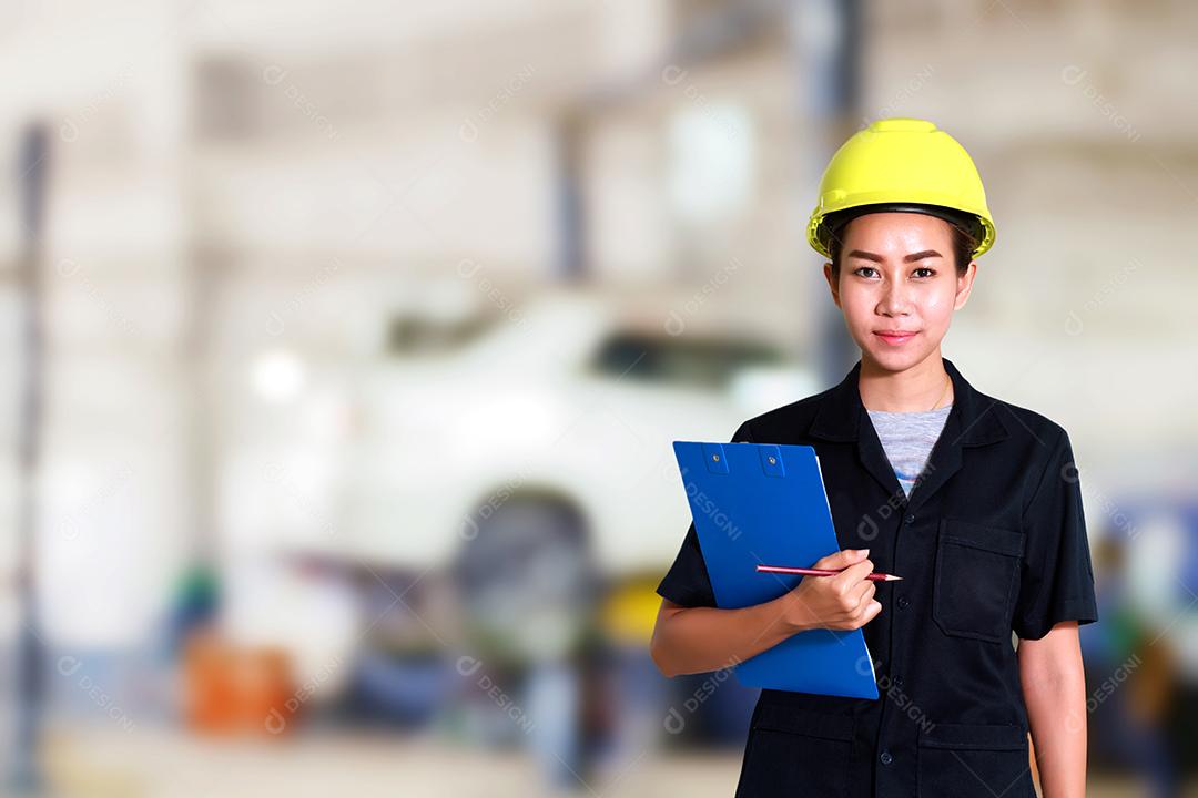 Retrato de uma jovem mecânica sorridente inspecionando um carro na oficina de automóveis