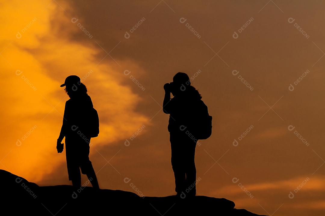 silhueta de mulheres asiáticas com mochila tirando uma foto no topo das montanhas